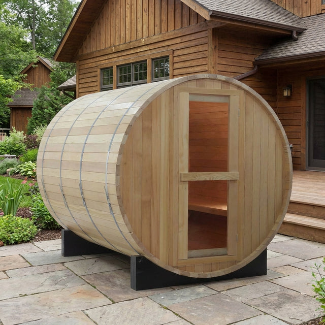 Wooden barrel sauna on a stone patio in front of a wooden house
