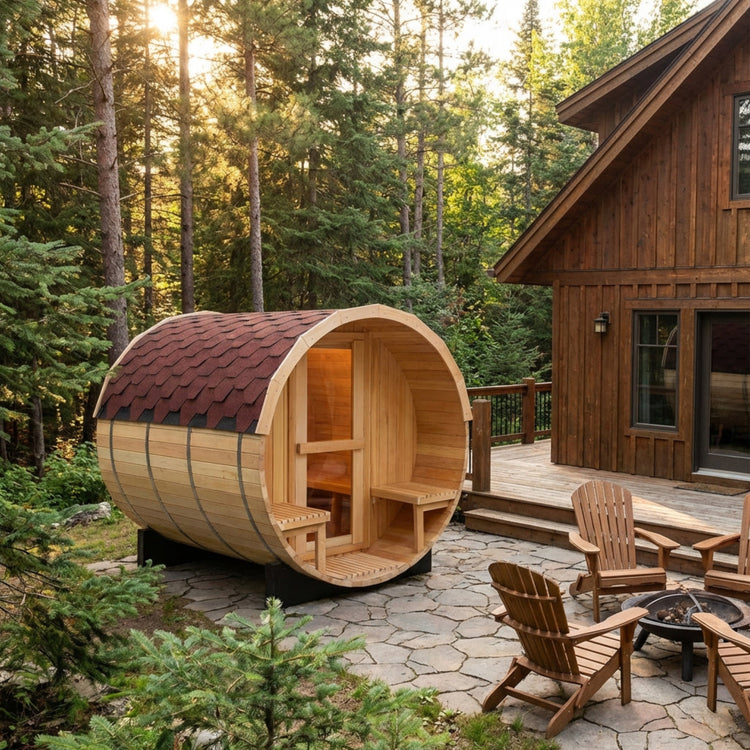 Wooden barrel sauna in a forest setting with a cabin and chairs.