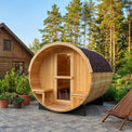 Wood barrel sauna in a garden setting with trees and a house in the background