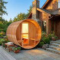 Wooden barrel-shaped sauna in front of a house with a stone chimney.